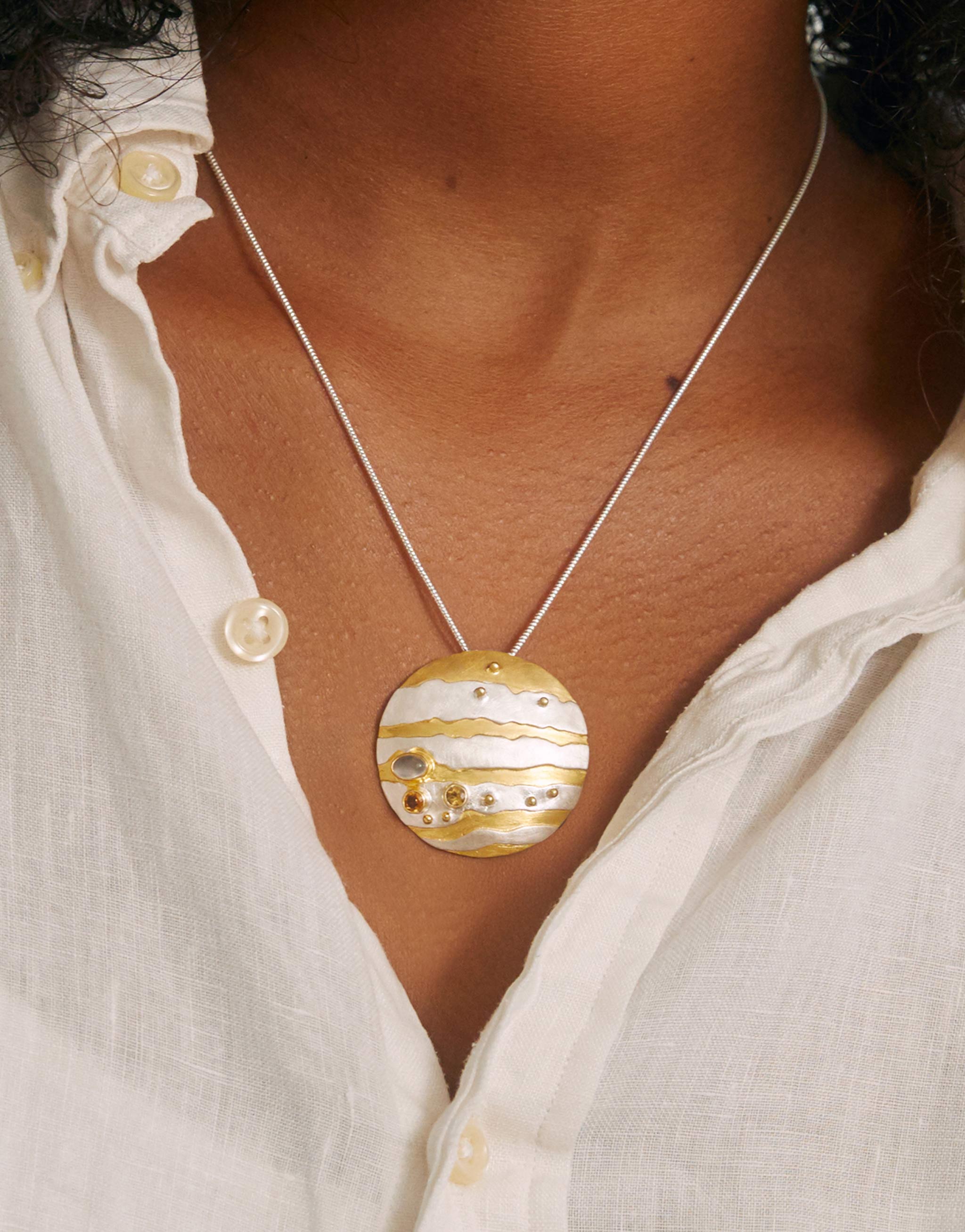 A Jupiter planet necklace with a silver chain, gold and silver pendant with moonstone and citrine.