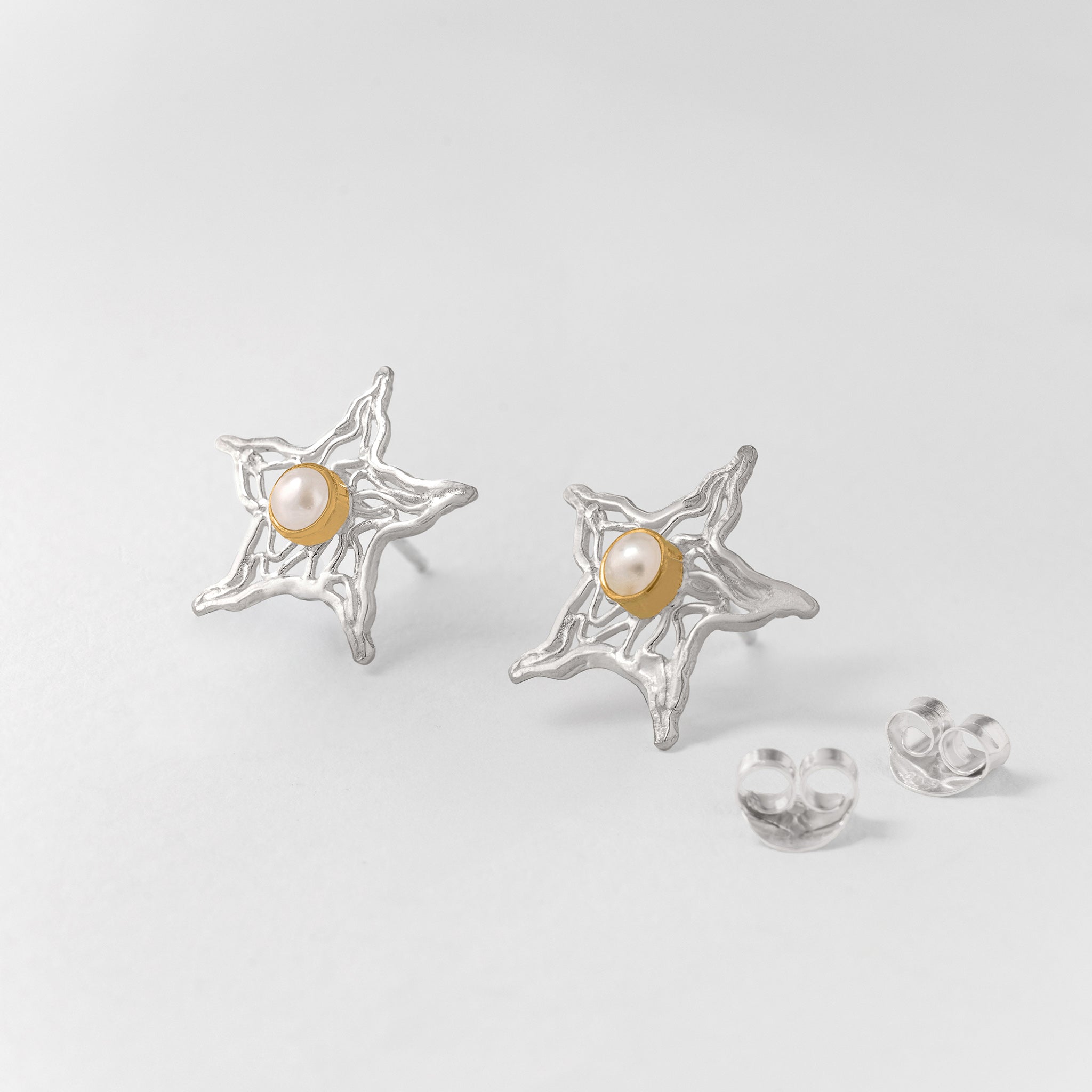 Sea star-shaped silver earrings with a single pearl and gold plate details.
