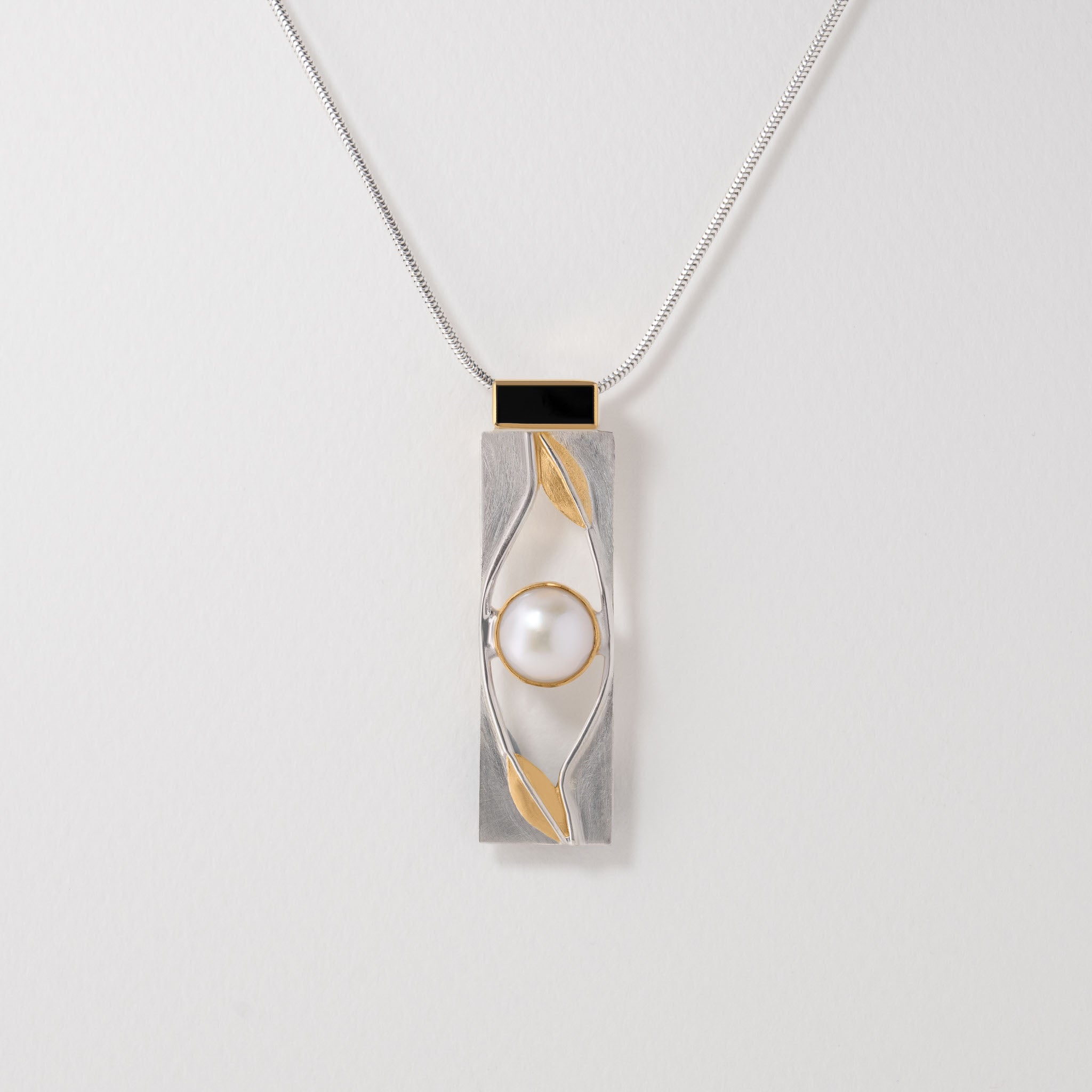 An Art Deco-inspired pendant necklace with a silver chain and a gold-colored pendant featuring geometric lines and a central pearl.