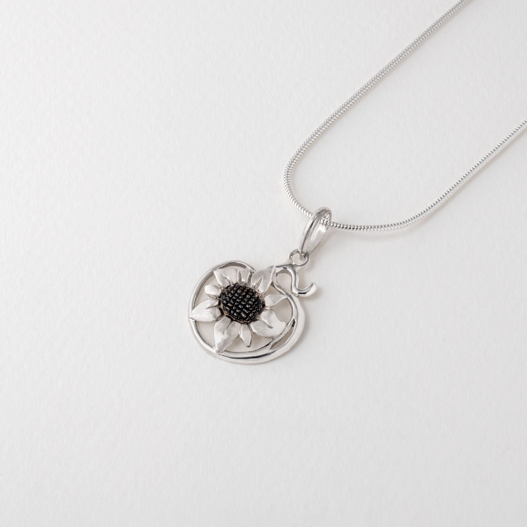 A silver necklace with a chain and a sunflower pendant in Van Gogh style