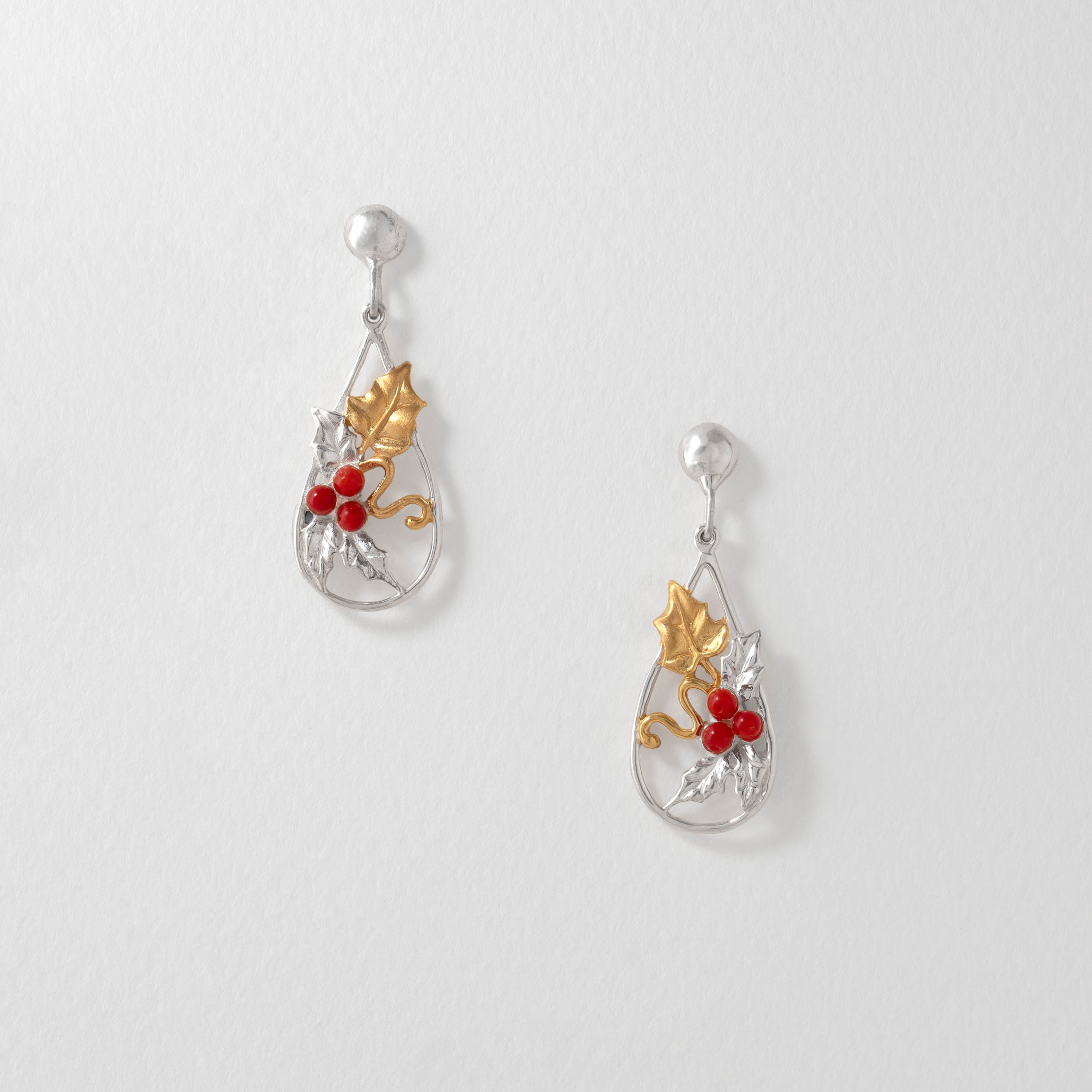 A pair of silver and gold teardrop-shaped earrings with holly leaves and red berries.