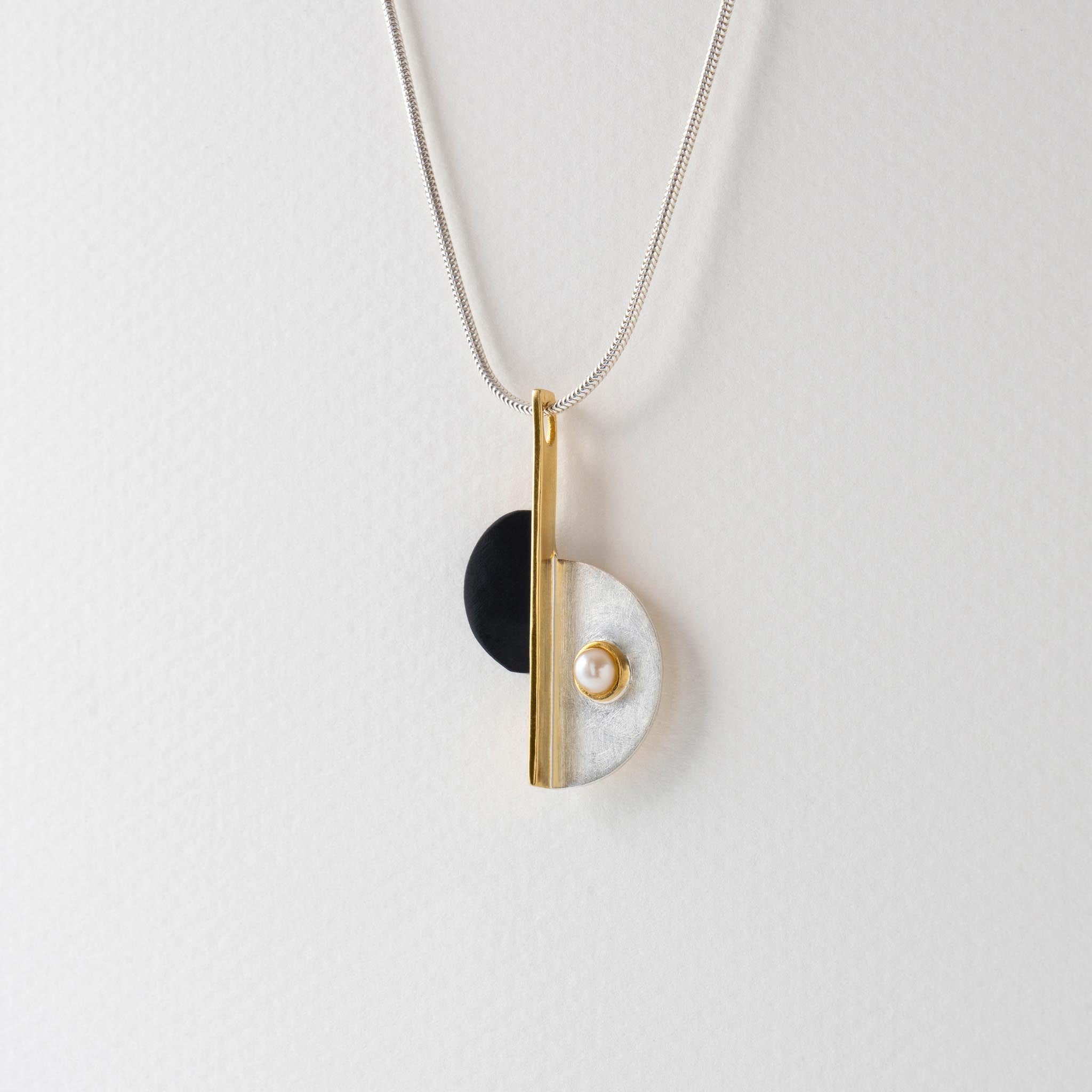 An Art Deco design necklace with a geometric black, gold, and silver pendant on a chain with pearl