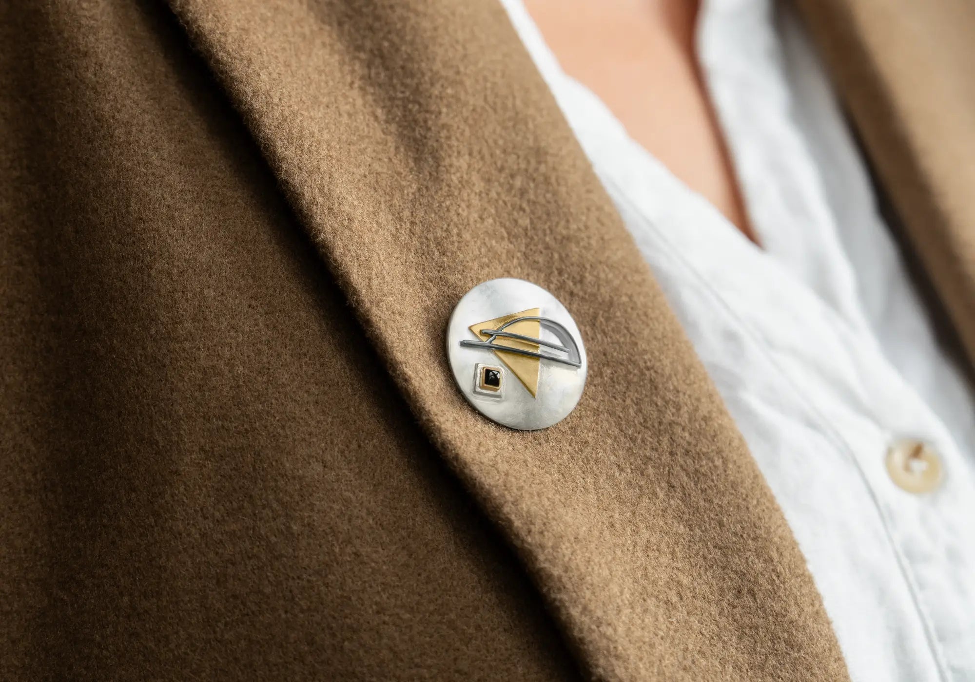 Close-up of a brown coat with a decorative Bauhaus brooch in silver and gold plate.