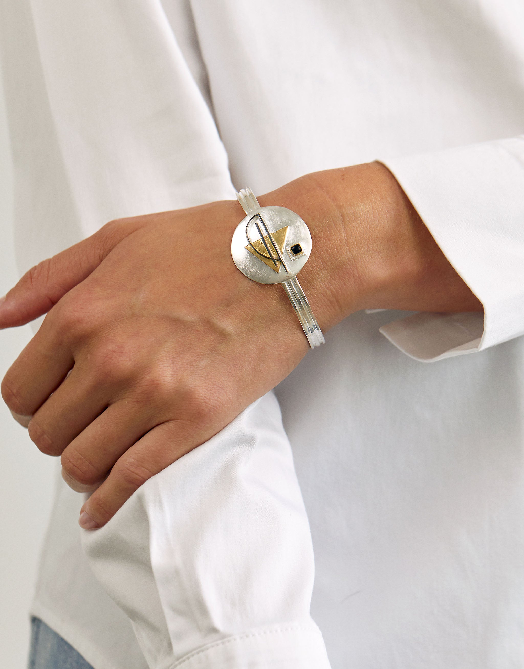 Bauhaus inspired sterling silver bangle with minimalist open cuff design, accented with 18ct gold plate and black onyx. Features bold geometric shapes that reflect the Bauhaus school’s clean lines and functional aesthetic.