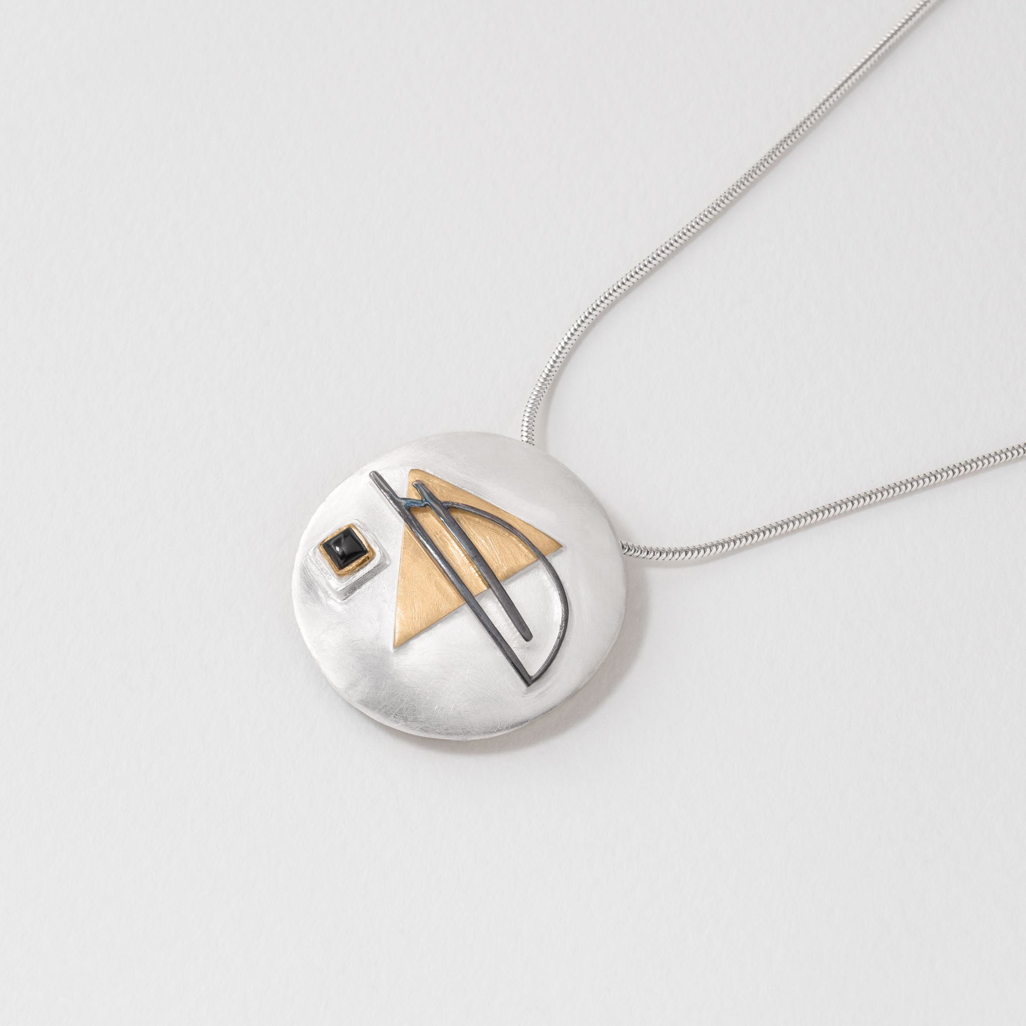 Bauhaus inspired 2-in-1 sterling silver brooch and pendant with geometric design. Features a triangular 18ct gold plated accent, black enamel line detail, and a small square black onyx stone.