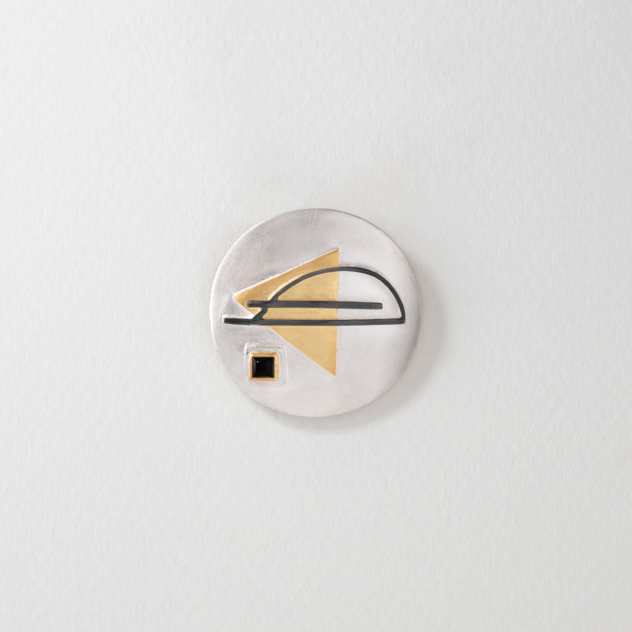 Bauhaus-inspired sterling silver brooch and pendant with a circular design. Features a geometric gold-plated triangle, black linear detailing, and a square black onyx accent, reflecting minimalist Bauhaus style.