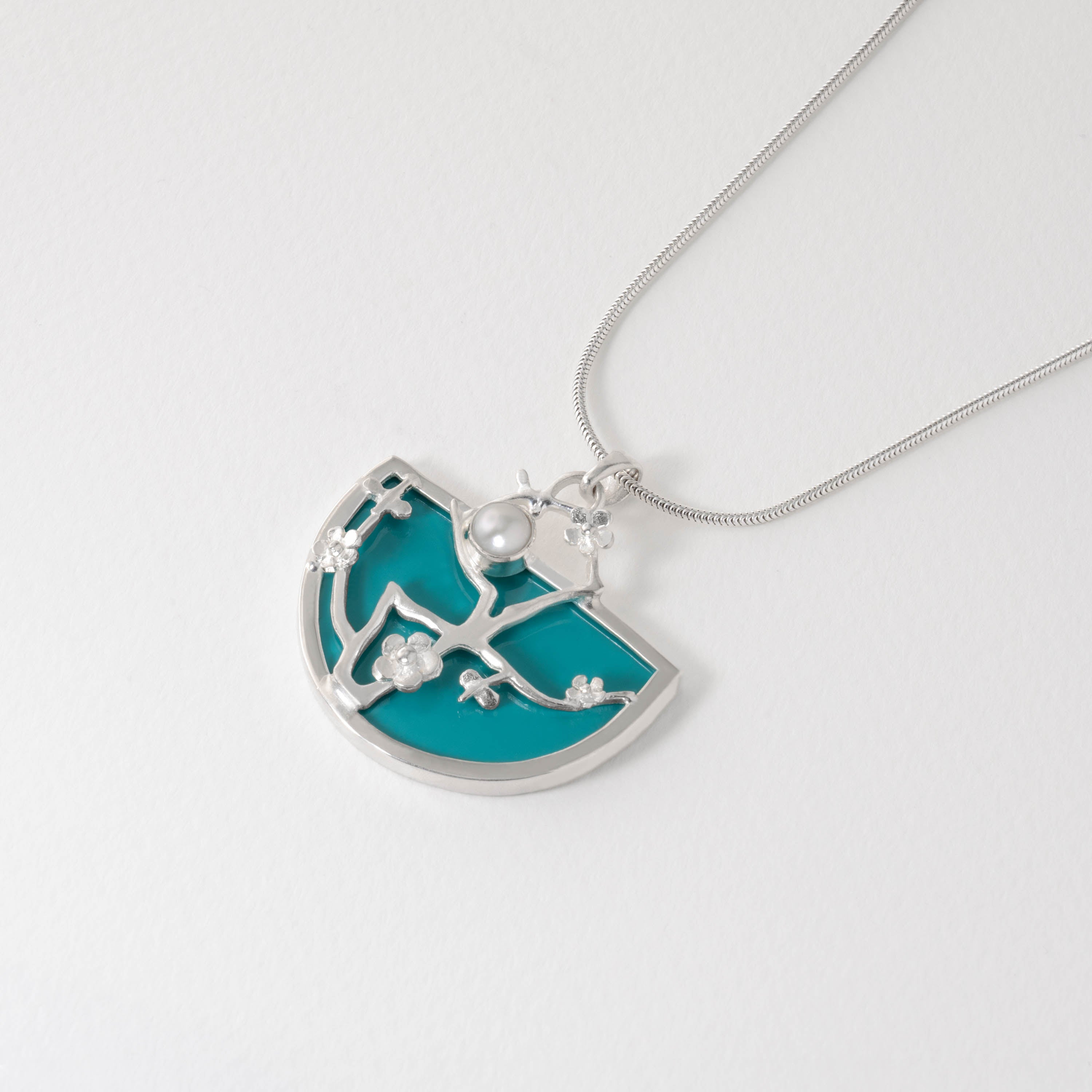 Sterling silver Almond Blossom necklace inspired by Van Gogh. A semi-circle pendant with turquoise blue resin background is overlaid with silver blossom branches and a pearl-like accent, reflecting impressionist artistry in jewellery form.