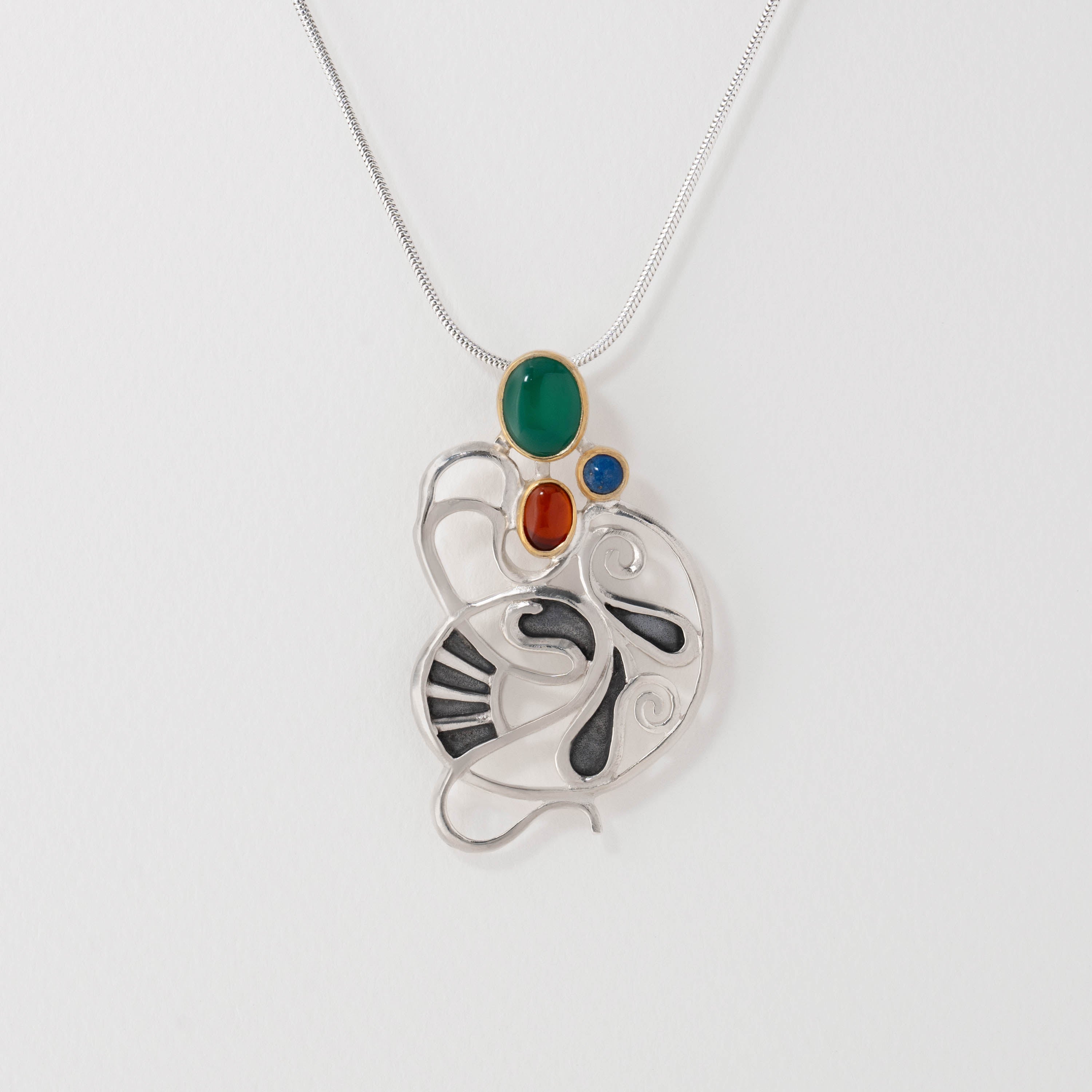 Gaudí inspired pendant necklace in sterling silver with green agate, amber and lapis lazuli. Featuring fluid curves and surrealist design, the pendant reflects Gaudí’s Catalan Modernist style and fusion of nature with artistry.