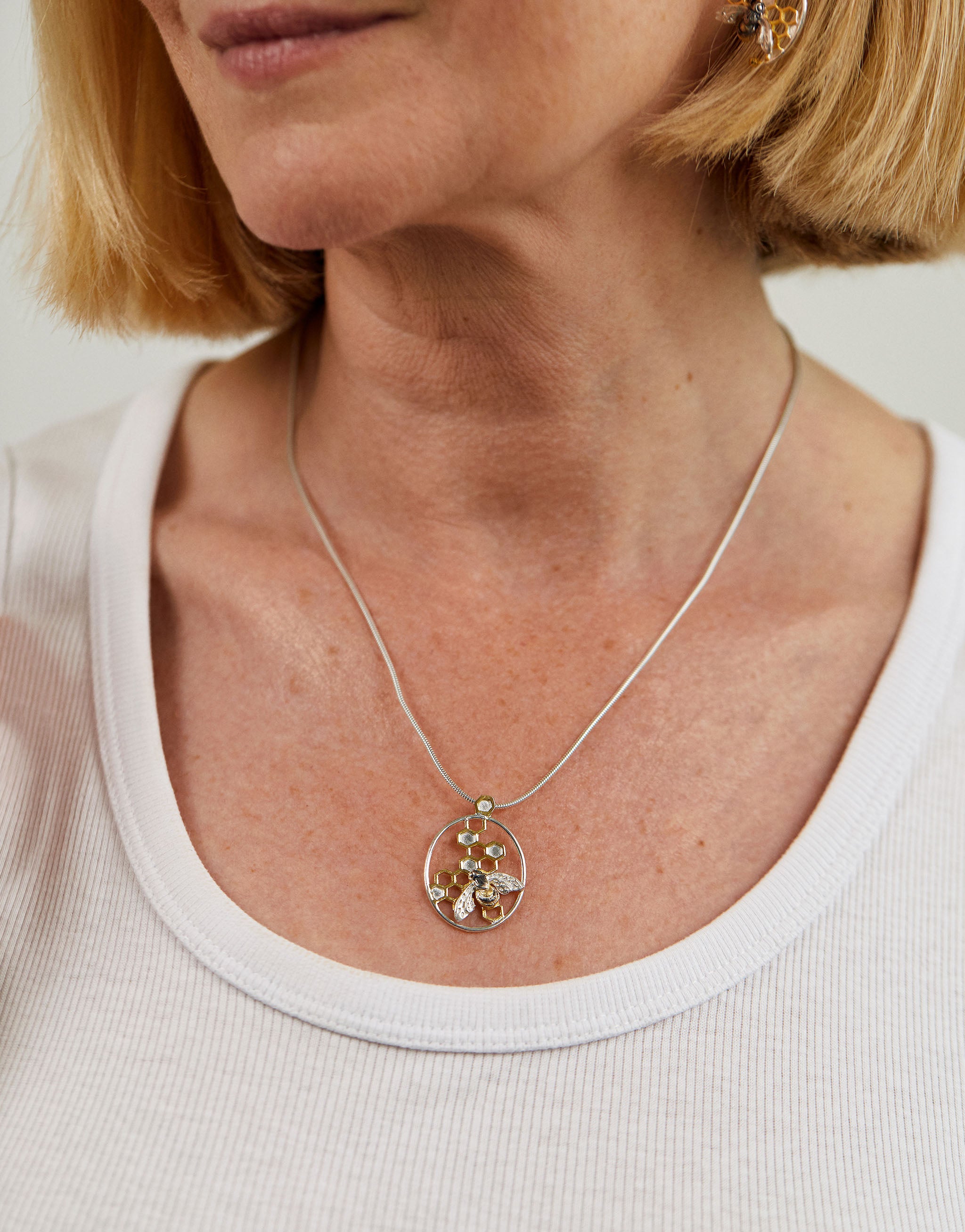 A  honeybee pendant necklace with intricate cutout honeycomb design in sterling silver and 18ct gold.