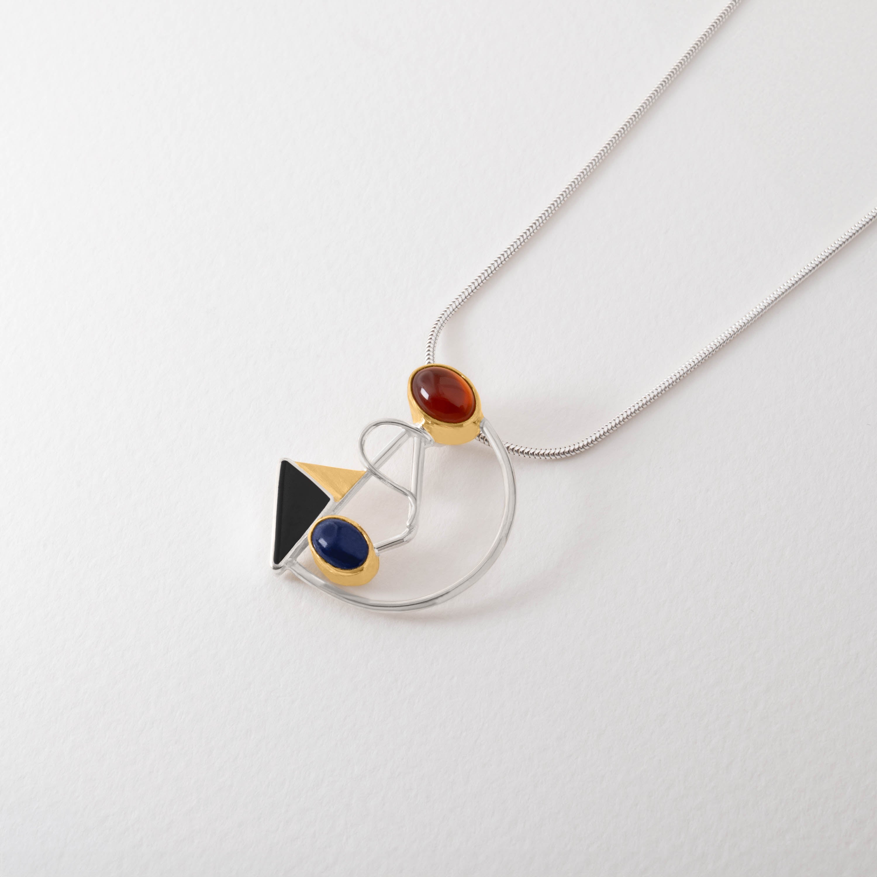 Kandinsky inspired pendant necklace in sterling silver with 18ct gold plate. The abstract design combines geometric shapes with gemstones—red carnelian, blue lapis lazuli and black onyx—echoing Kandinsky’s bold use of colour and form.