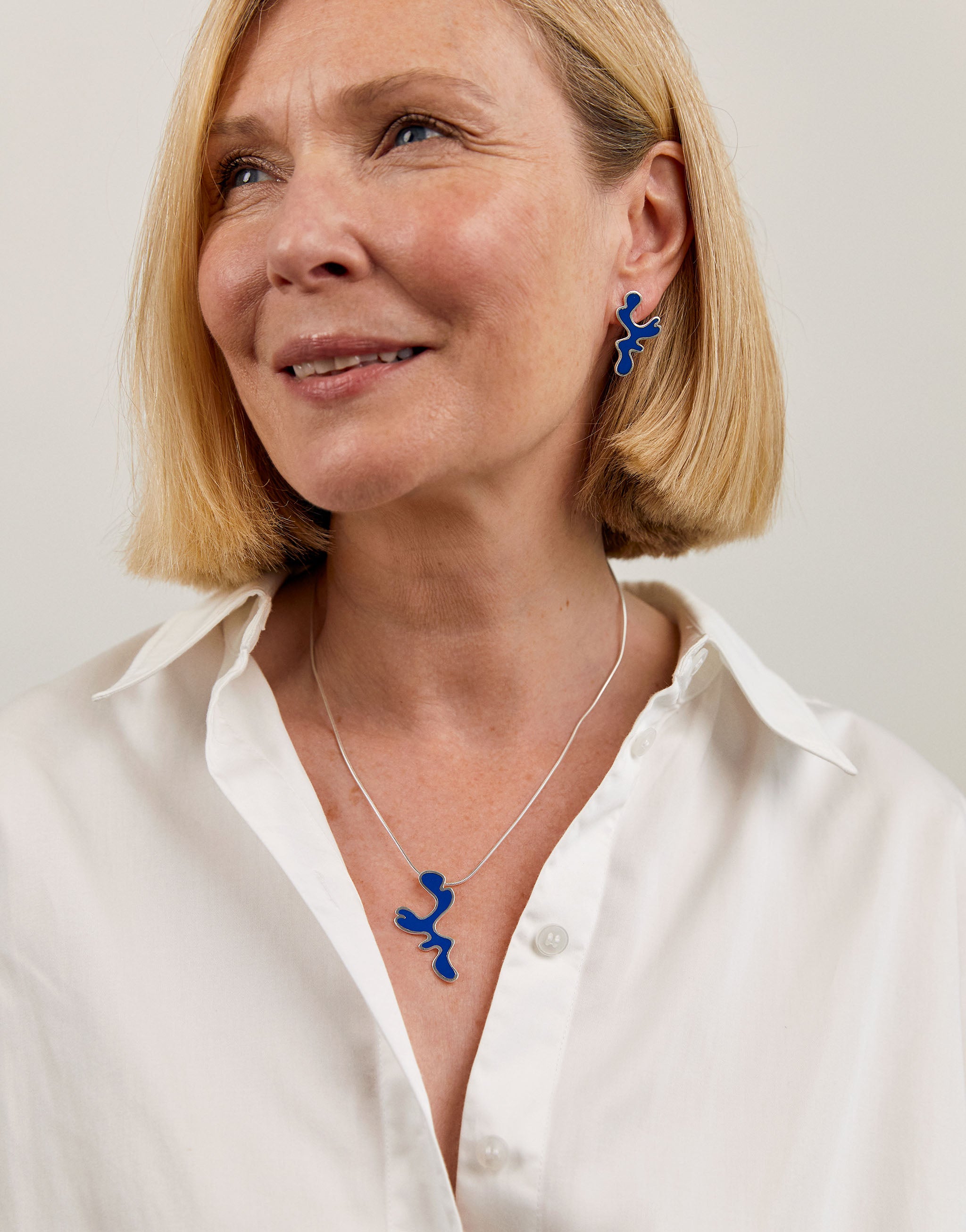 A woman wearing a blue geometric Matisse-patterned necklace and earrings.