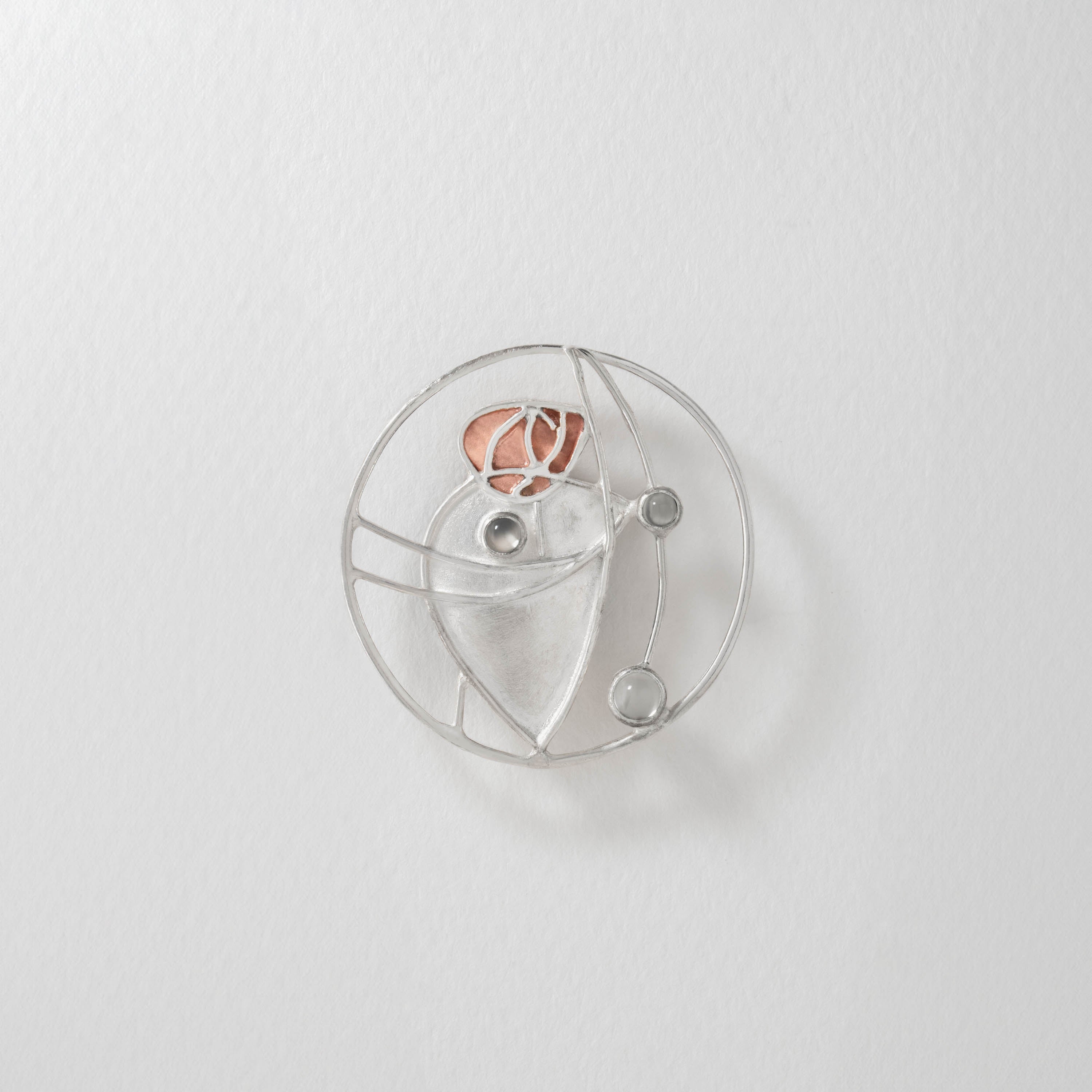 Charles Rennie Mackintosh inspired brooch in sterling silver with warm copper accents. The elegant Art Nouveau design reimagines his stained-glass patterns, centred with a luminous moonstone for a timeless statement.