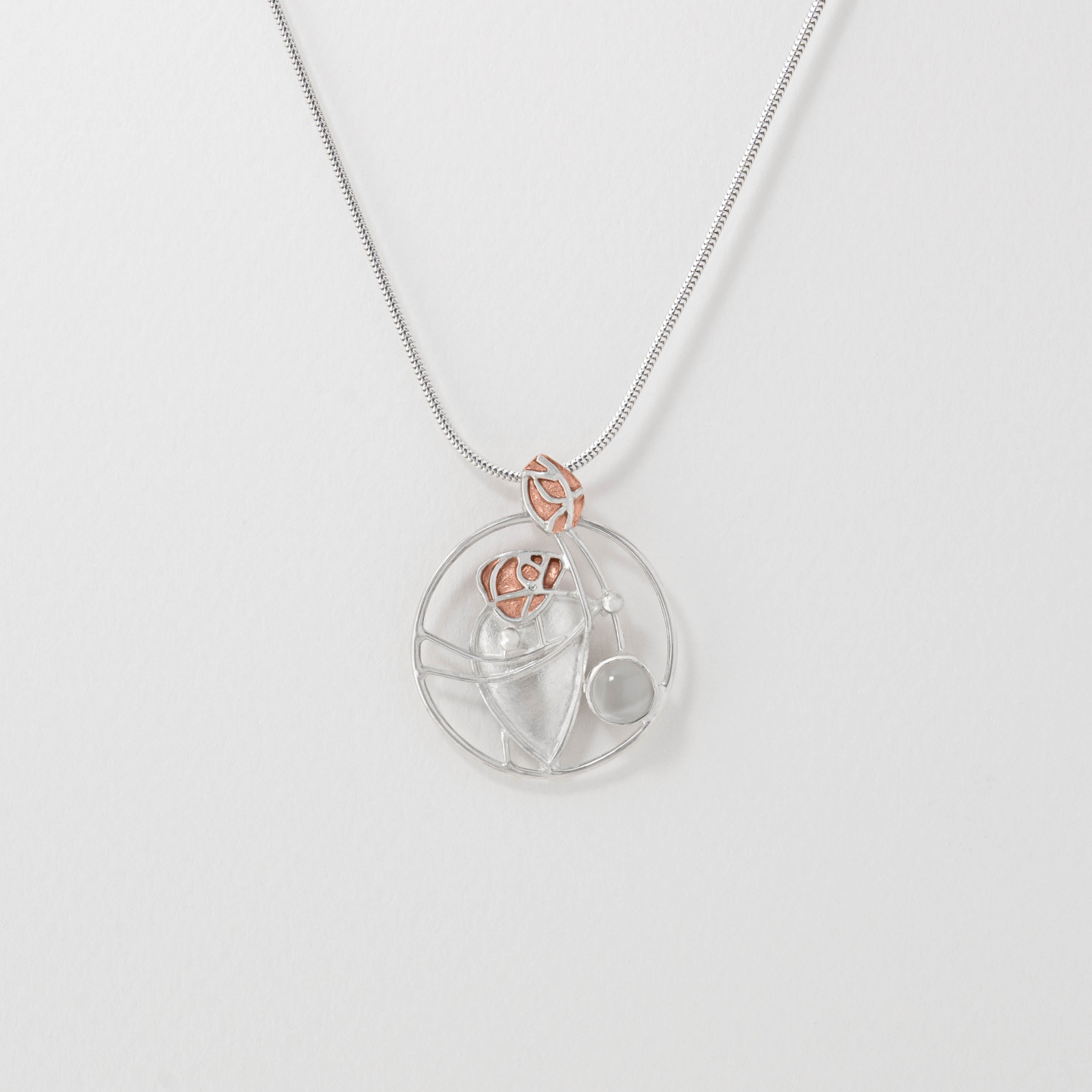 A round moonstone pendant with a silver flowing design and warm copper accents, attached to a silver chain.