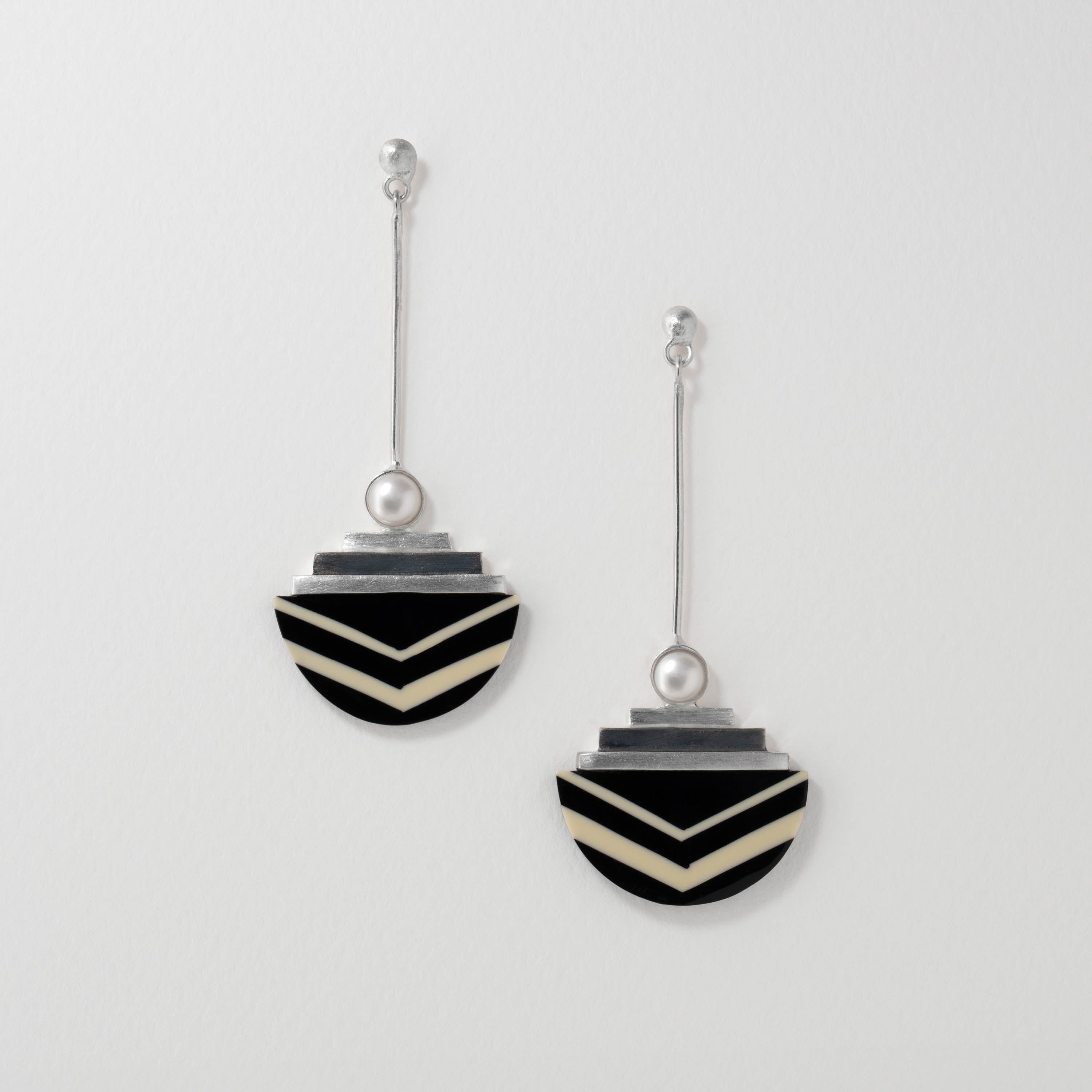 A pair of earrings with a geometric black and white resin design, silver details, and a natural pearl accent.