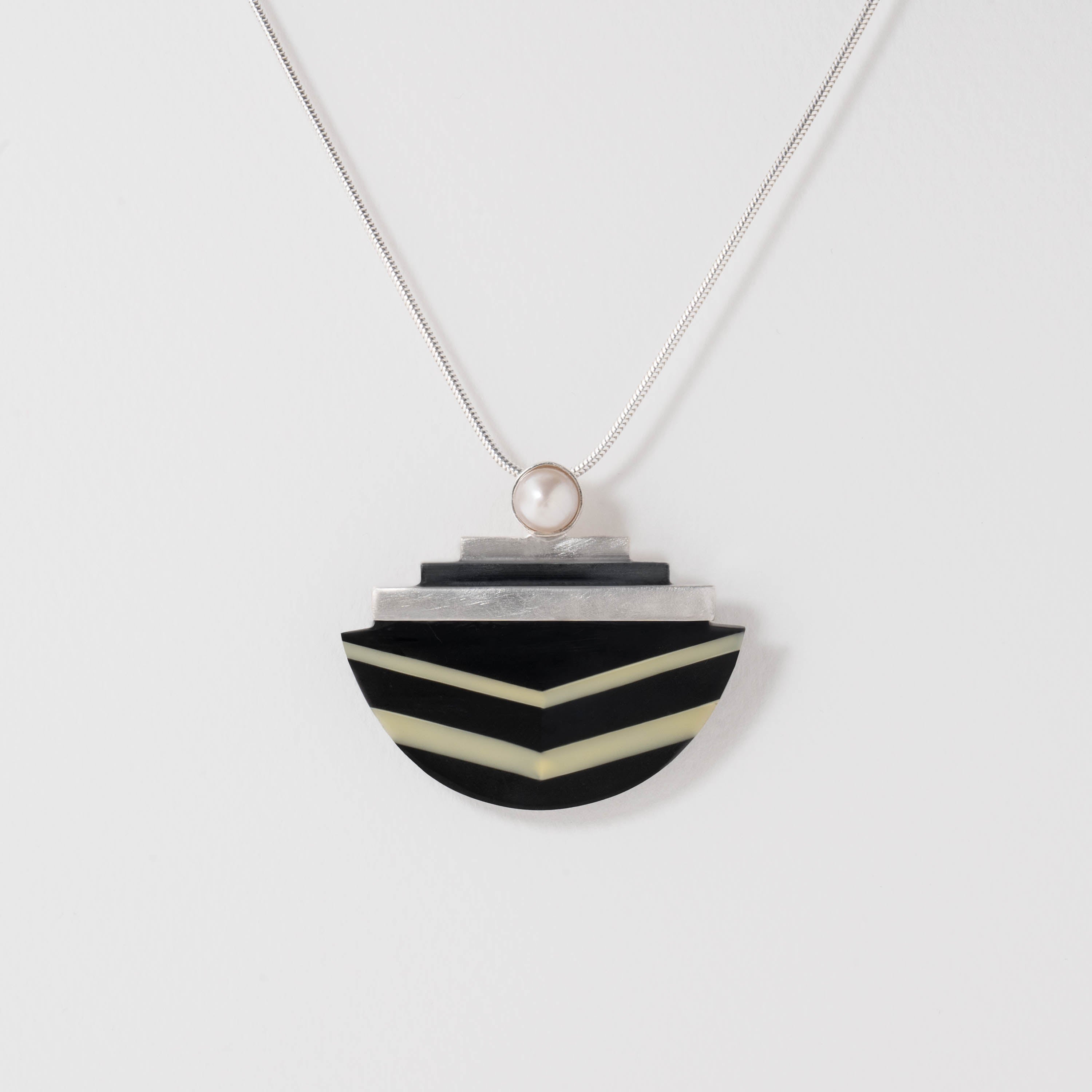 Geometric Wiener Werkstätte pendant necklace crafted in sterling silver with black and white resin. A natural pearl tops the stepped silver design, showcasing the movement’s modernist balance of bold form and refined simplicity.
