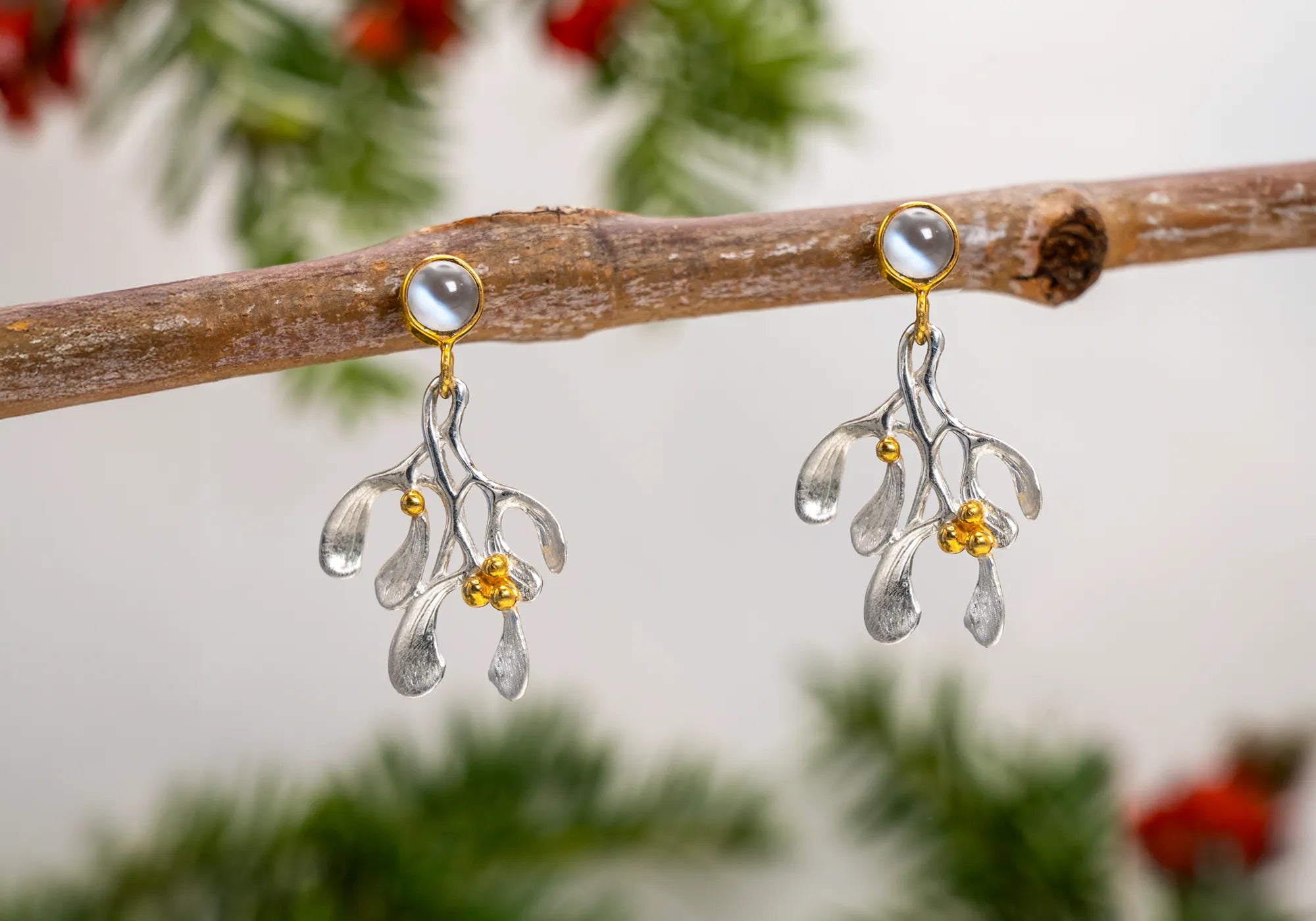 Silver, gold, and moonstone Christmas earrings with a mistletoe design, set against a festive backdrop.