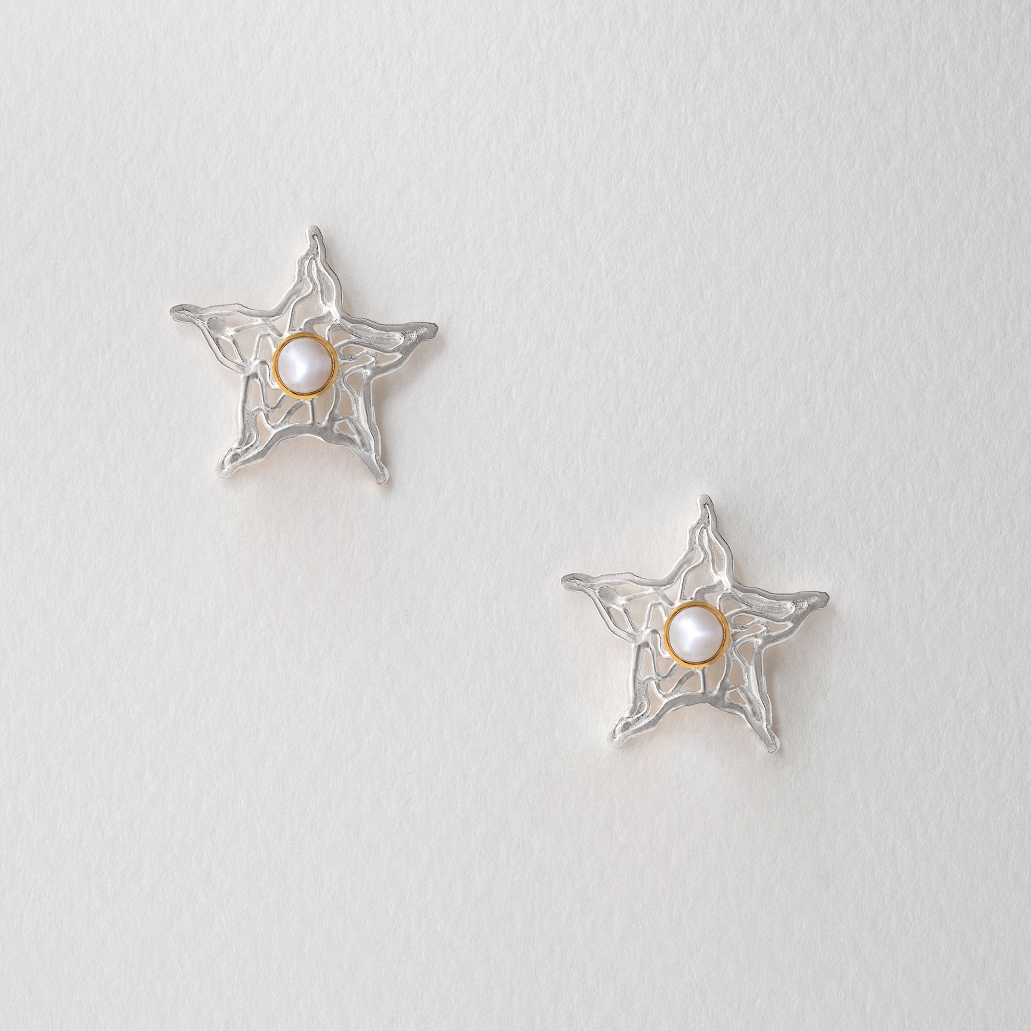 Star-shaped silver earrings with a central pearl with gold plate settings.