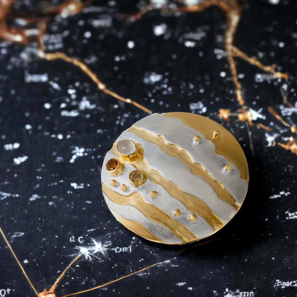 Gold and silver planet-like silver brooch  on a starry night sky background.